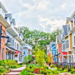 Row of colorful, red, yellow, blue, white, green painted residential townhouses, homes, houses with brick patio gardens in summer