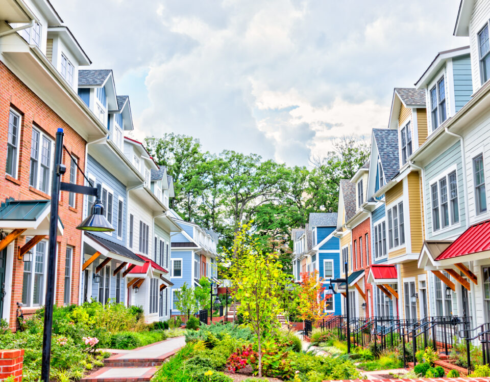 Row of colorful, red, yellow, blue, white, green painted residential townhouses, homes, houses with brick patio gardens in summer