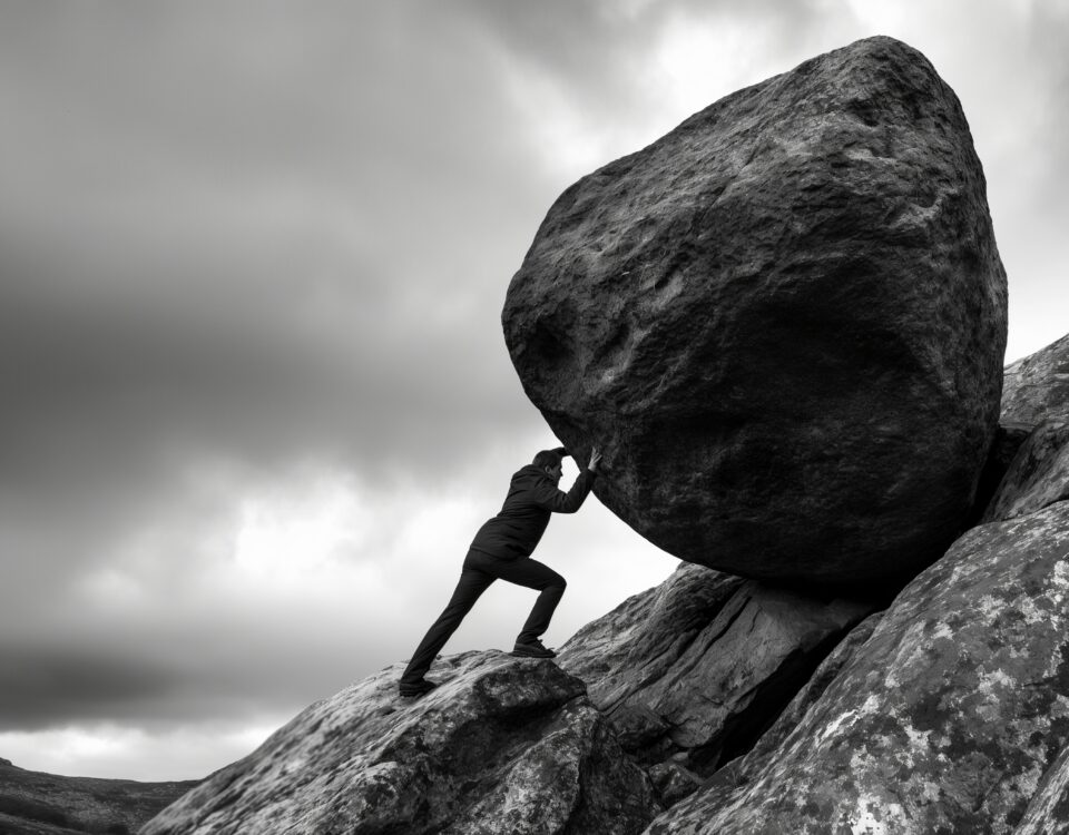 Silhouette man struggles to push massive boulder uphill on rocky terrain image. Overcast sky, rugged landscape photography scene wallpaper. Sisyphean task resilience concept photo